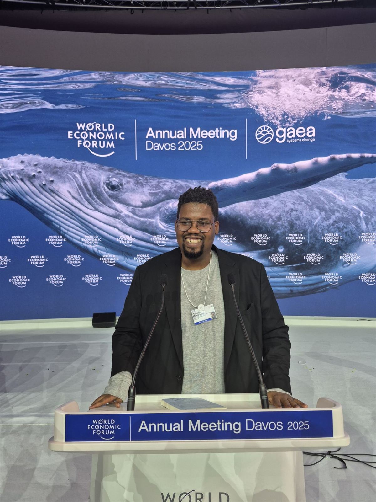 Gilberto Morishaw standing at the World Economic Forum podium in Davos, a large image of a whale behind him
